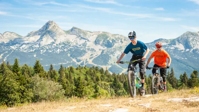 Due ciclisti in abbigliamento sportivo che percorrono una strada di montagna con paesaggi innevati sullo sfondo