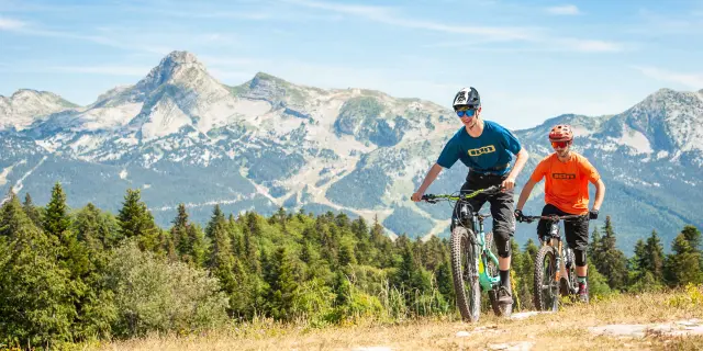 Due ciclisti in abbigliamento sportivo che percorrono una strada di montagna con paesaggi innevati sullo sfondo