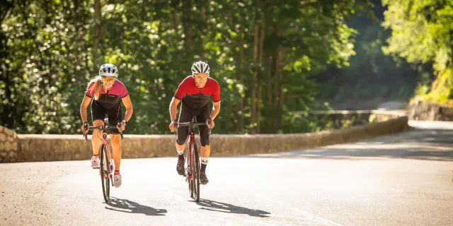 Due ciclisti in abbigliamento rosso e casco giallo che percorrono un sentiero forestale