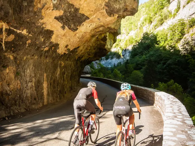 Due ciclisti in abbigliamento sportivo che percorrono una strada di montagna fiancheggiata da scogliere
