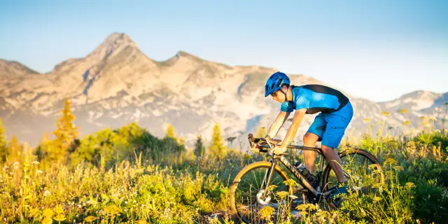 Ciclista con casco blu e giacca fluorescente su una bicicletta da montagna in terreno accidentato