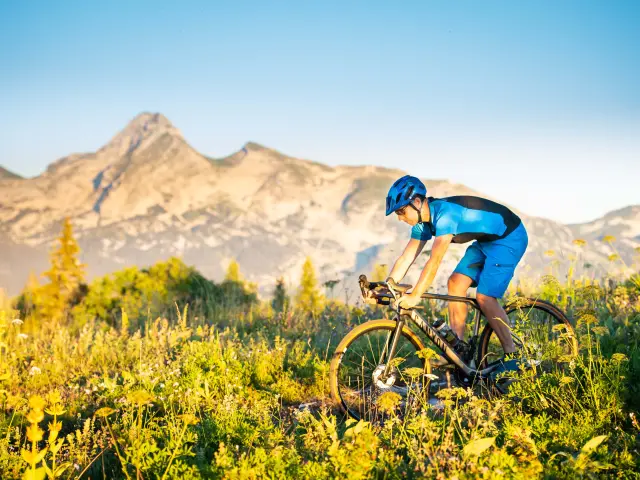 Cycliste portant un casque bleu et une veste fluorescente sur un vélo de montagne en terrain accidenté