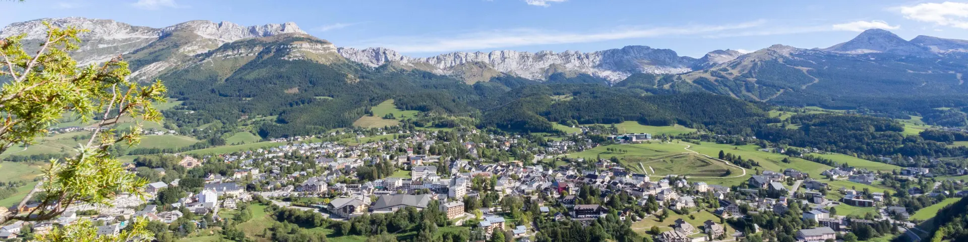 Paesino circondato da colline verdi sotto un cielo blu con nuvole bianche