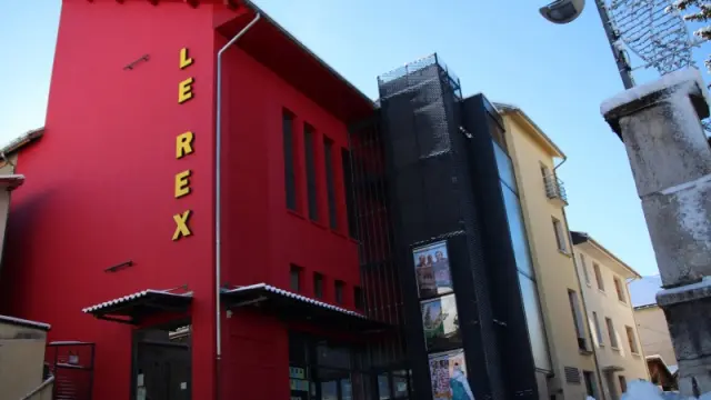 Façade rouge d'une librairie nommée Rex sous la neige, avec des bâtiments en arrière-plan