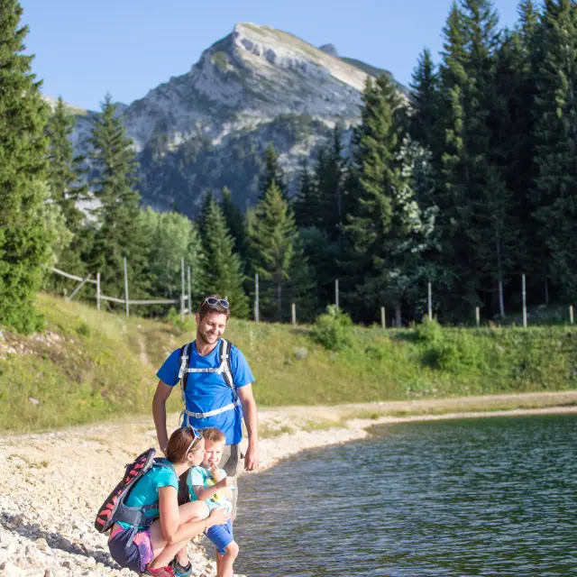 Child in blue and pink swimsuit running on a pebble beach by a mountain lake