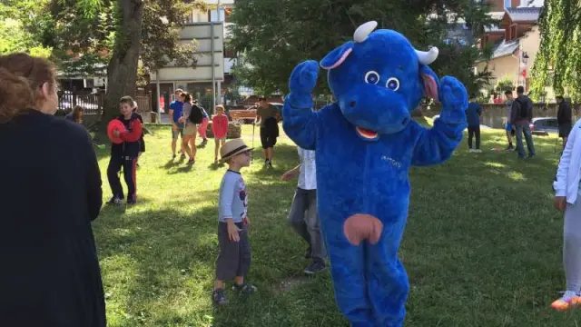 Enfant vêtu d’un costume de dinosaure bleu à capuche, debout dans un parc vert