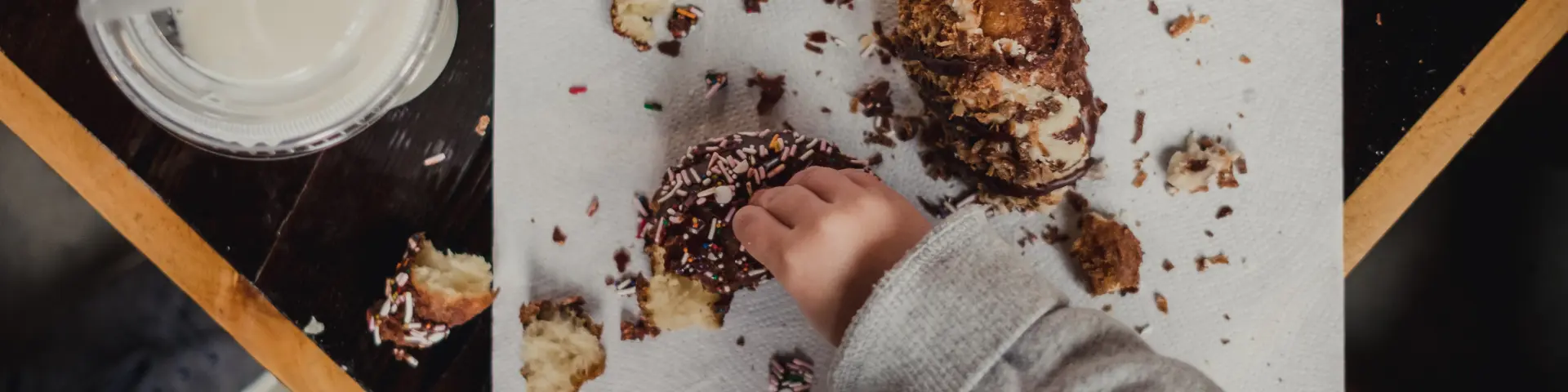 Main tenant un cookie recouvert de pépites de chocolat et de noix, posé sur une plaque de cuisson