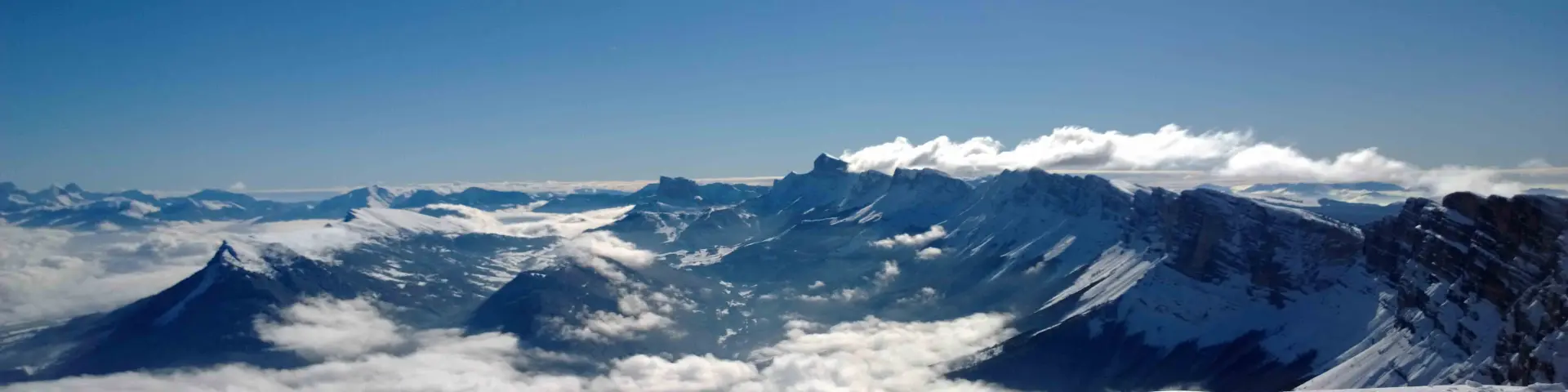 Montagnes enneigées avec des vallées et des crêtes rocheuses sous un ciel bleu clair