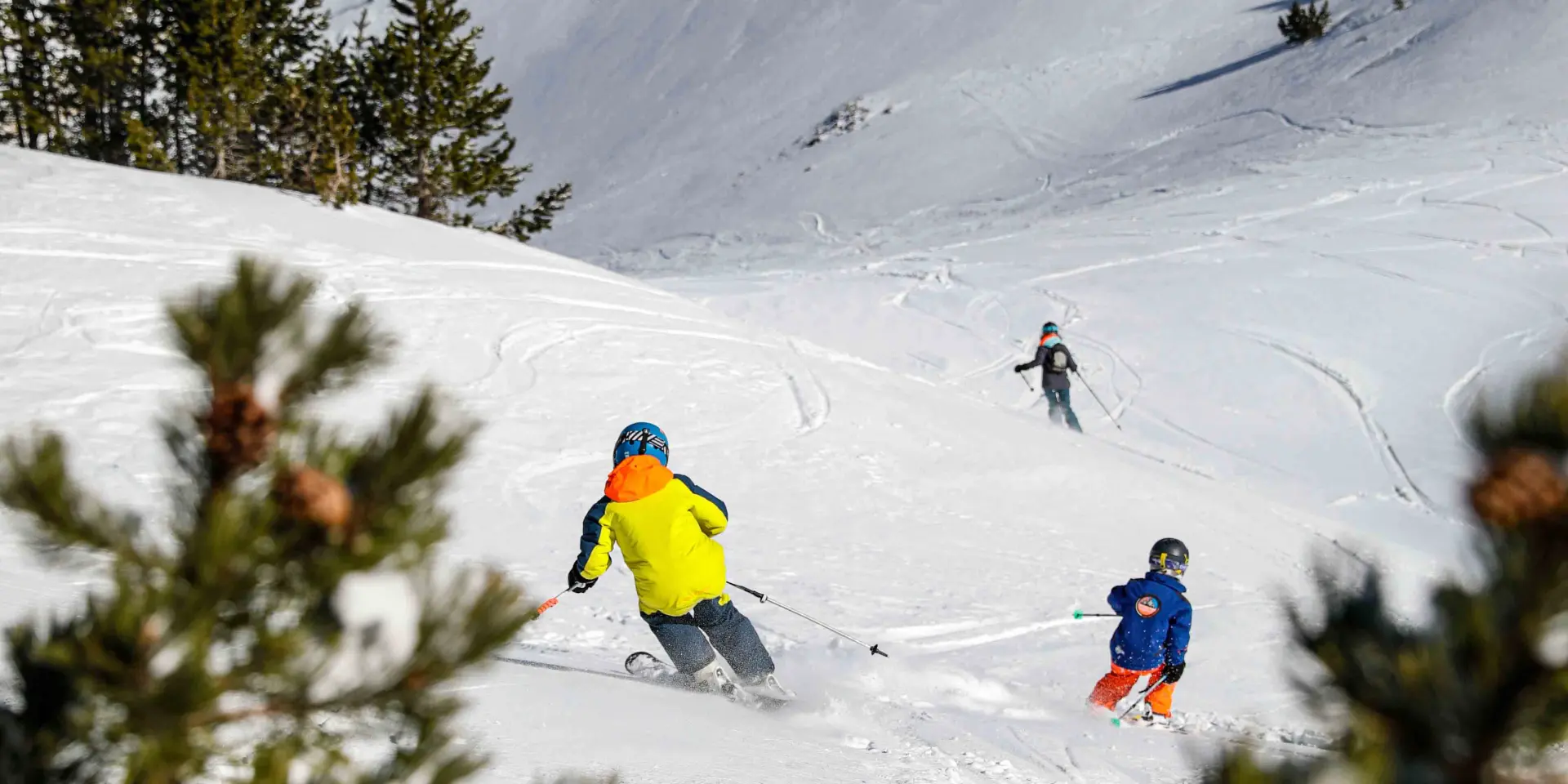 Due sciatori in abbigliamento colorato su una pista da sci innevata, con abeti sullo sfondo