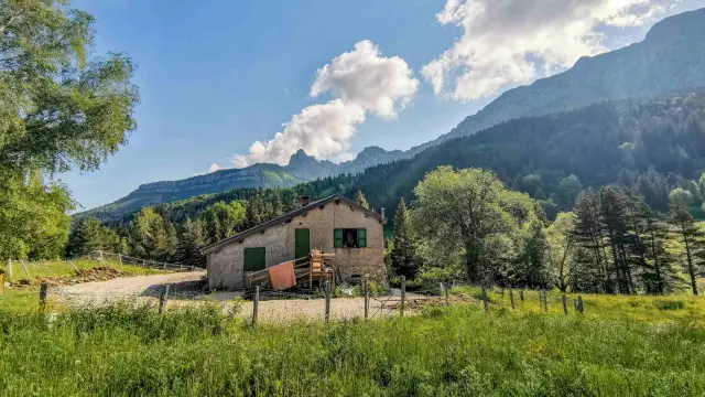 Casa in legno e pietra circondata da vegetazione con montagne sullo sfondo