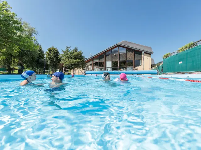 Piscine extérieure avec toboggan en plastique vert, plongeoir et enfants jouant dans l’eau