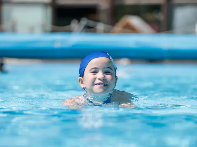 Enfant portant des lunettes de natation bleues et un bonnet de bain, nageant dans une piscine