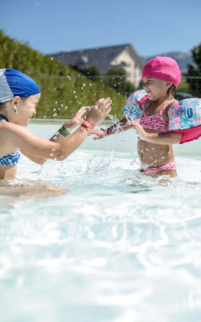 Deux enfants, l’un en maillot de bain bleu et l’autre en maillot à motifs colorés, jouent dans l’eau peu profonde d’une plage