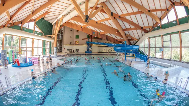 Indoor pool with wooden vaults, swimmers, and terraces along the edge