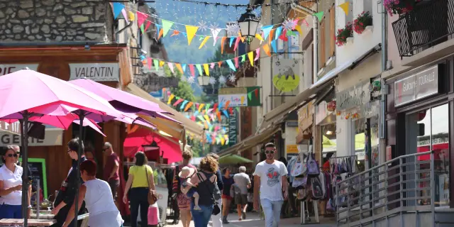 Rue commerçante avec guirlandes lumineuses et passants sous des parasols roses