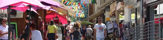 Shopping street with colorful garlands and pedestrians under pink umbrellas