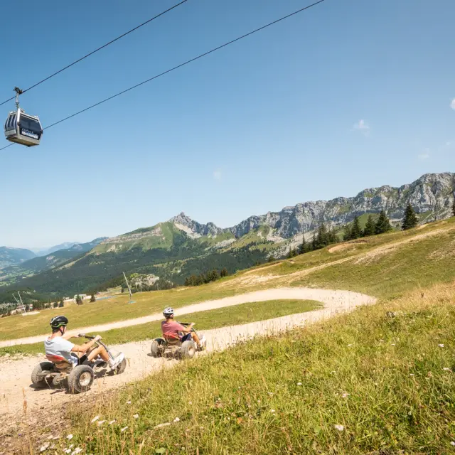 Deux motards en train de rouler sur une route sinueuse en montagne, avec un parapentiste en vol au-dessus d'eux