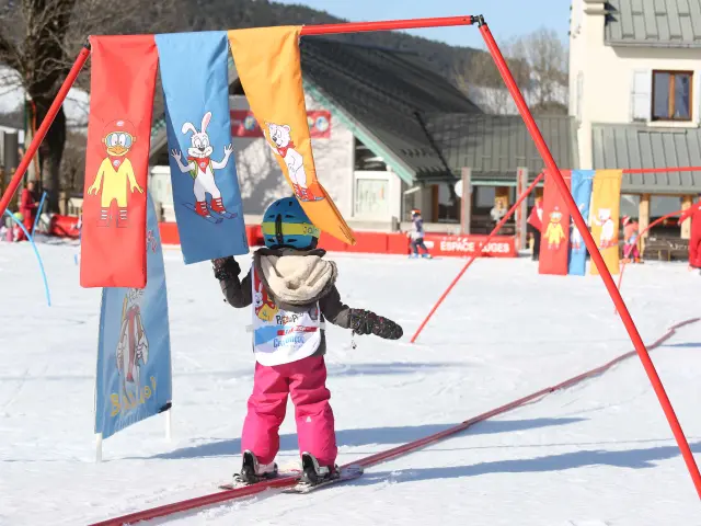 Bambino in tuta da sci rosa e blu che scende una pista da sci con bandiere colorate