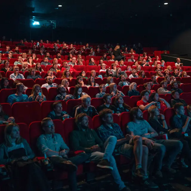 Audience seated in a concert hall lit by blue and red spotlights