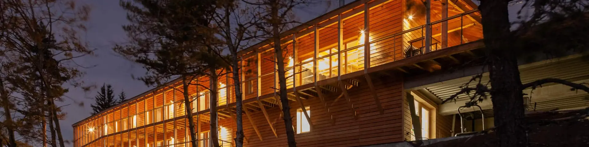 Chalets en bois alignés avec des fenêtres éclairées, entourés d’arbres, au crépuscule