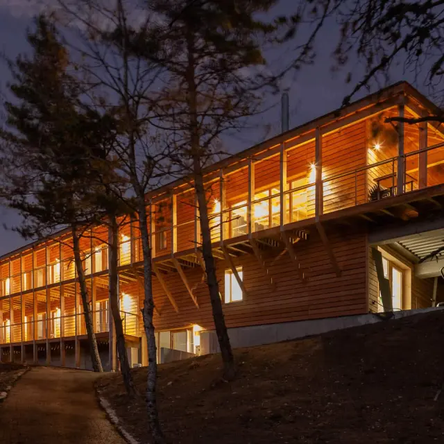 Chalets en bois alignés avec des fenêtres éclairées, entourés d’arbres, au crépuscule