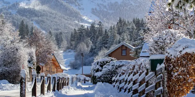 Chalet en bois entouré de neige avec des sapins enneigés et une montagne en arrière-plan au crépuscule