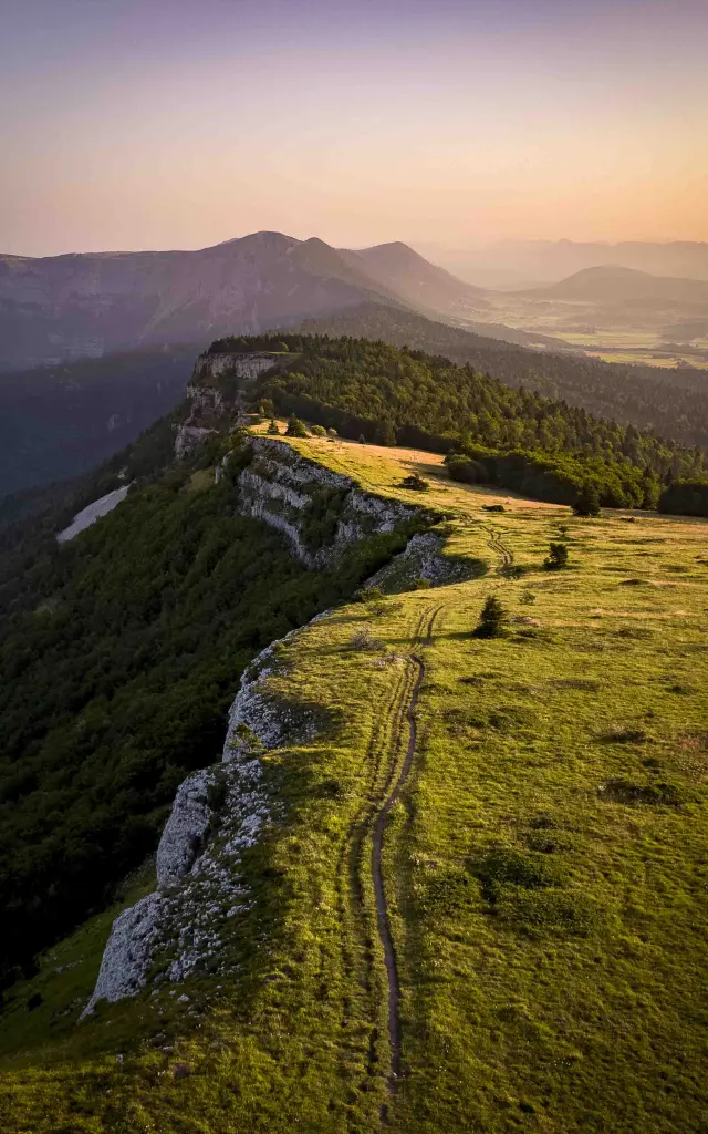 Hiking trail in the mountains lined with rocks and vegetation, lit by the last rays of the sun