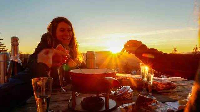 Donna seduta a un tavolo di una terrazza in riva al mare che guarda il tramonto