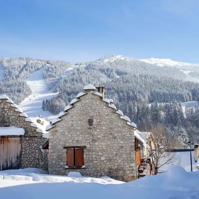 Petite maison en pierre avec cheminée et porte en bois sous la neige