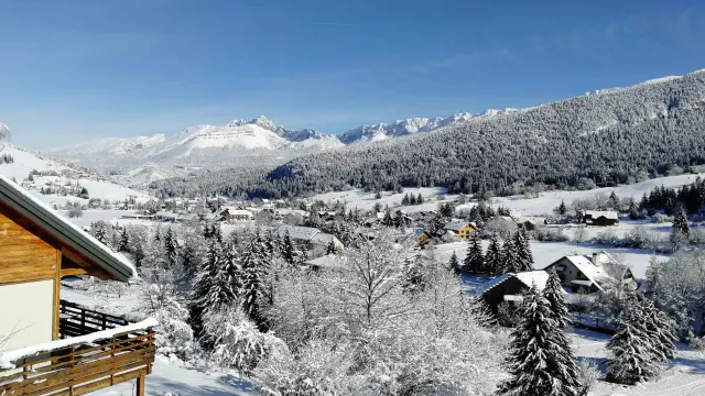 Vista di un villaggio di montagna innevato con chalet e abeti sotto un cielo blu chiaro