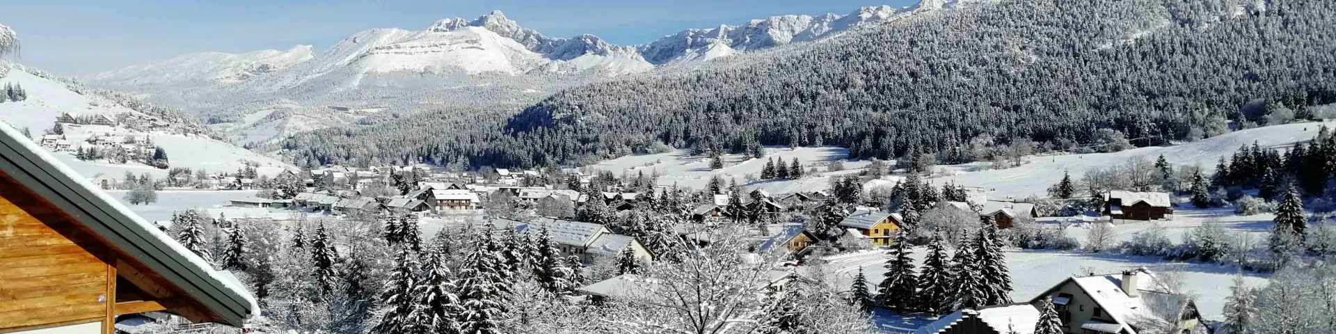 View of a snowy mountain village with chalets and fir trees under a clear blue sky
