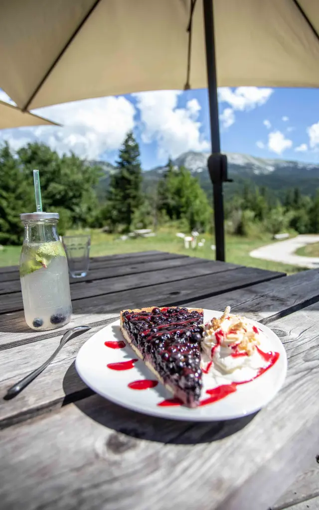 Assiette de dessert chocolaté avec sauce rouge et crème, posée sur une table en terrasse avec une bouteille d'eau et un verre