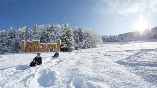 Due sciatori seduti su una pista innevata con bastoncini da sci, sotto un cielo sereno