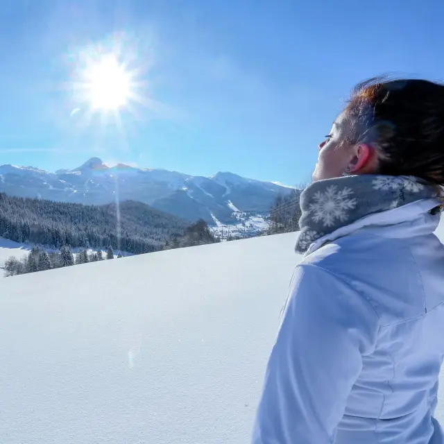 Escursionista in abbigliamento invernale che osserva un lago ghiacciato circondato da montagne innevate