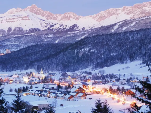 Village de montagne enneigé entouré de sommets enneigés au crépuscule