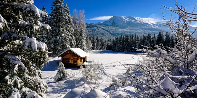 Cabine en bois isolée dans un paysage enneigé avec des montagnes en arrière-plan