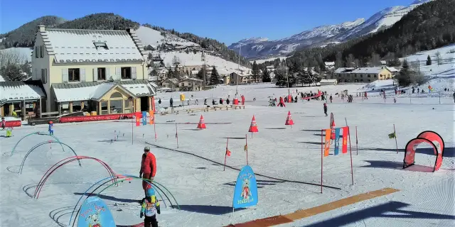 Station de ski avec des bâtiments en bois, des pistes damées et des drapeaux orange et bleu