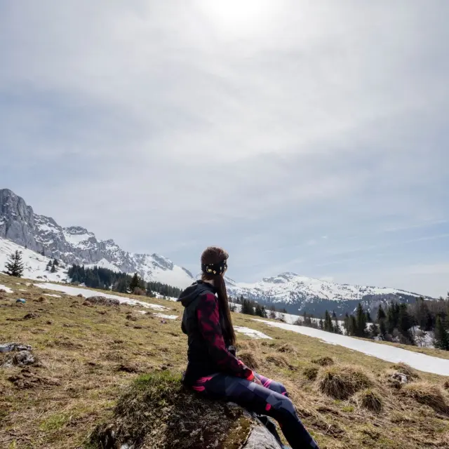 Persona in abbigliamento da escursionismo in piedi su un sentiero di montagna, con cime innevate sullo sfondo