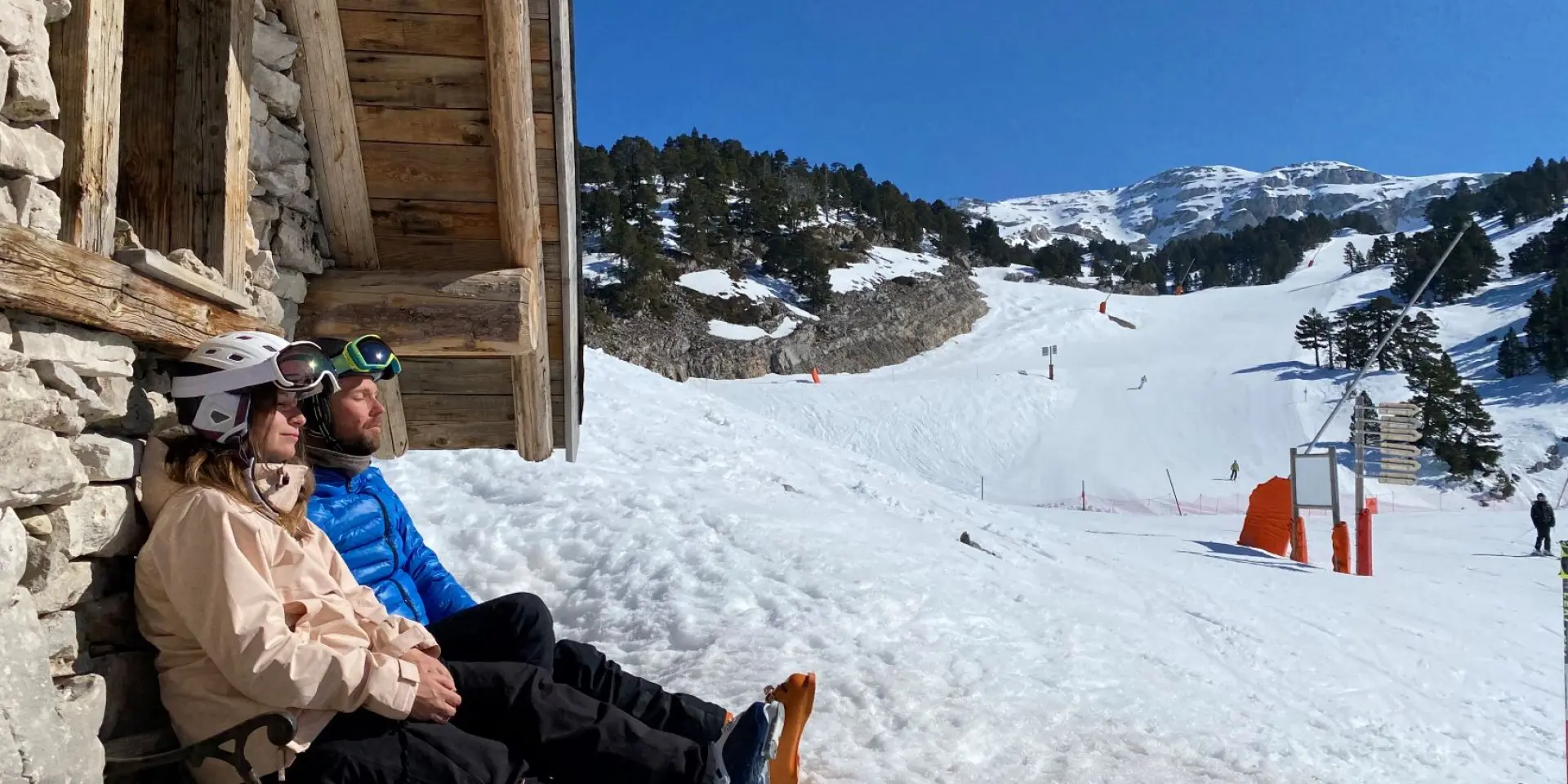 Due persone sedute su una panchina di pietra in montagna, con cime innevate sullo sfondo