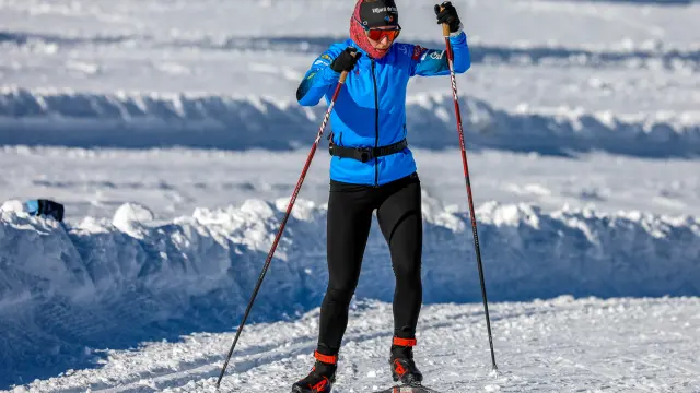 Skieuse debout sur des skis en position de descente, équipée d’un casque et de lunettes, sur une piste enneigée avec des montagnes en arrière-plan