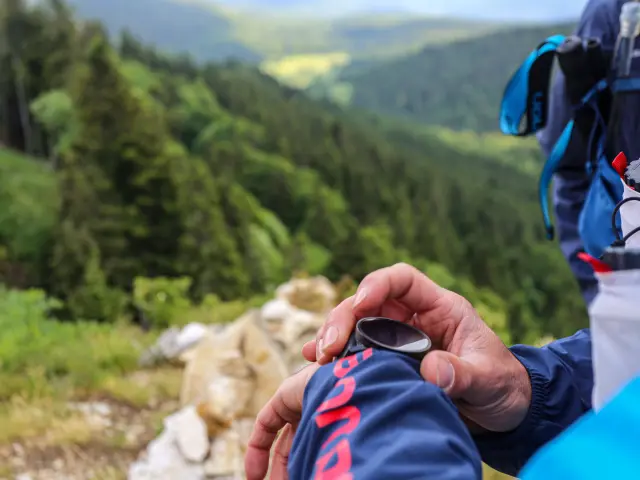 Mano che tiene un telefono cellulare con schermo acceso all'aperto, in montagna