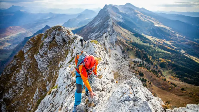 Randonneur vêtu d’un gilet orange et d’un pantalon bleu escaladant une paroi rocheuse en montagne