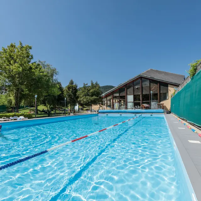Piscine rectangulaire bleue entourée de terrasses en bois et de végétation