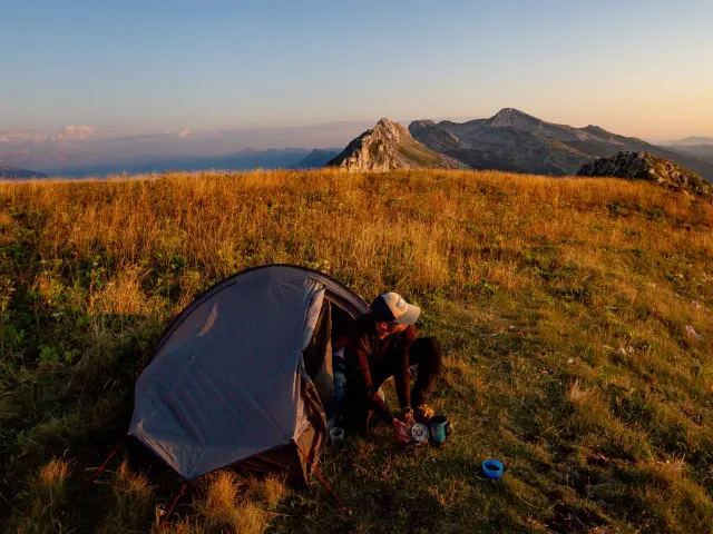 Tente bleue et sacs de randonnée posés sur un promontoire rocheux au coucher du soleil