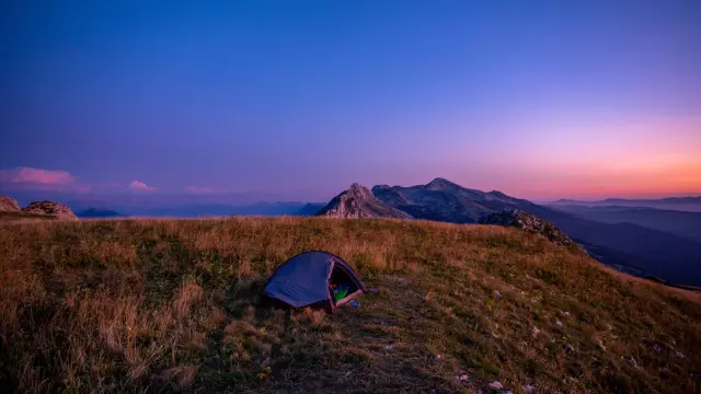 Tente bleue installée sur une colline avec un coucher de soleil en arrière-plan