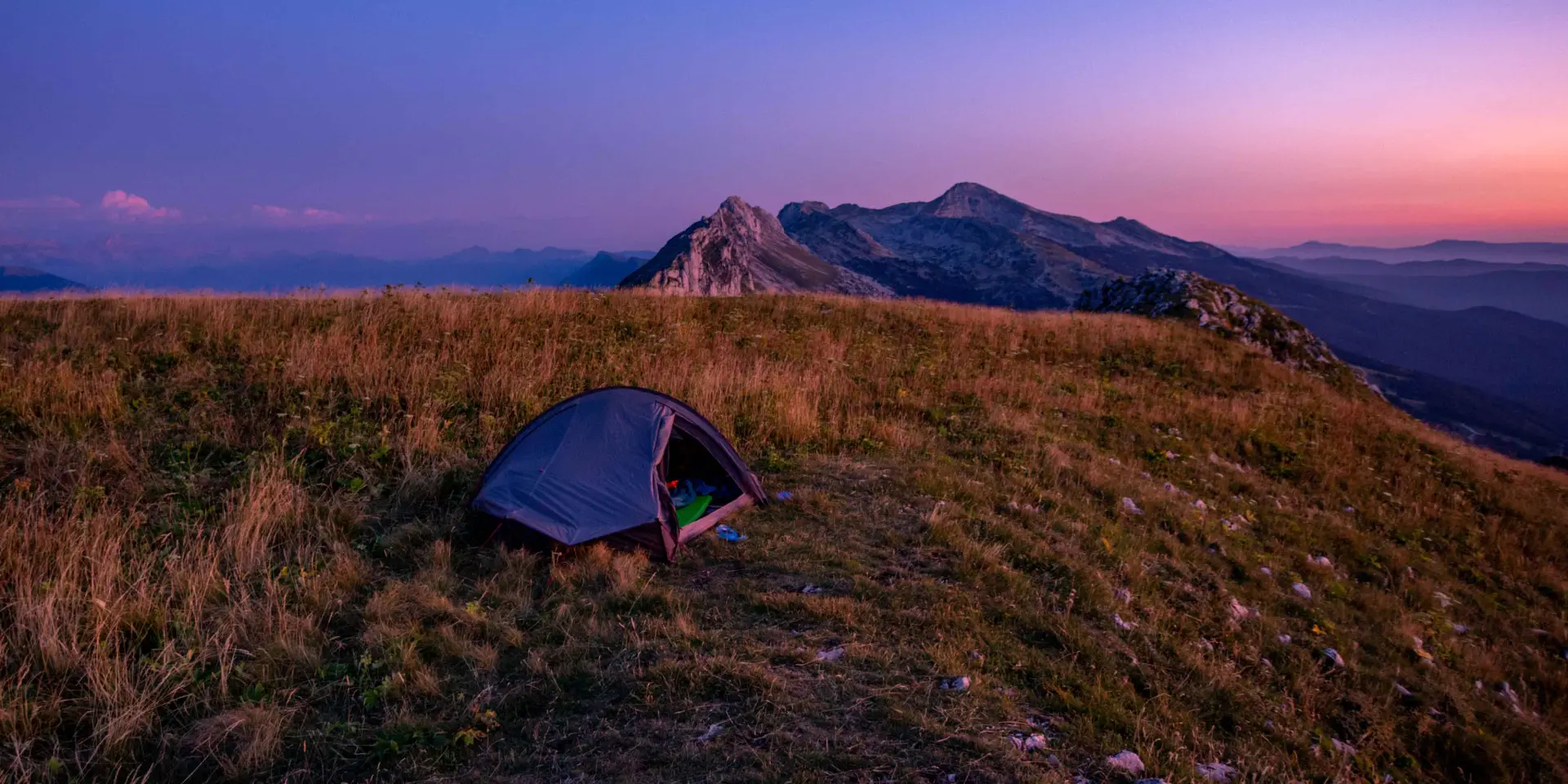 Tente bleue installée sur une colline avec un coucher de soleil en arrière-plan