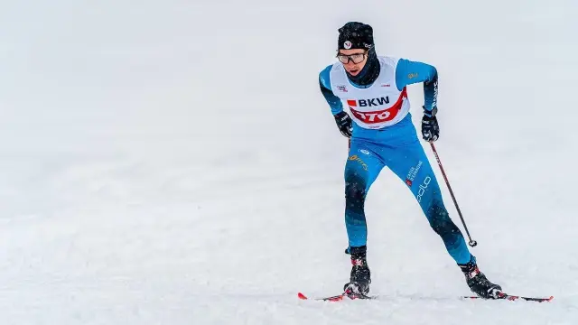 Sciatore in tuta blu e nera, casco e occhiali, in posizione di discesa su una pista da sci