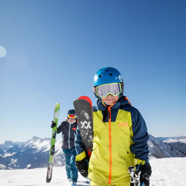 Trois skieurs en tenue de ski colorée sur une piste enneigée avec des montagnes en arrière-plan