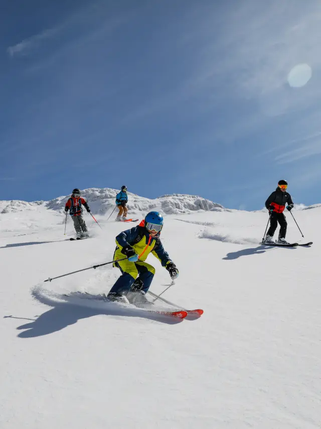 Deux enfants skiant côte à côte sur une piste enneigée sous un ciel dégagé