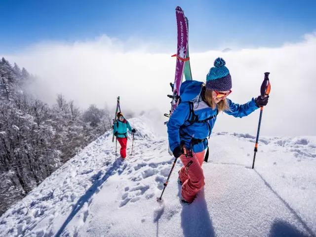 Deux enfants en tenue de ski descendent une piste enneigée, l'un avec des skis roses et l'autre avec des skis bleus